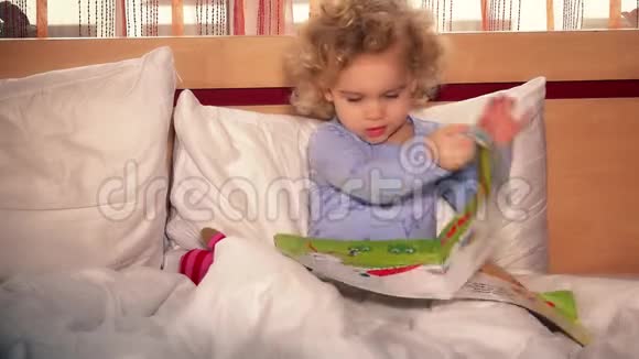 可爱的小女孩坐在床上看书幼儿独自在卧室视频的预览图