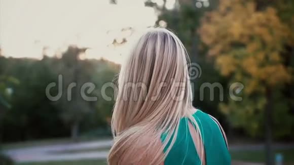 日落时公园里年轻的金发女人的后景女孩在风中挥动着她的头和头发慢动作视频的预览图