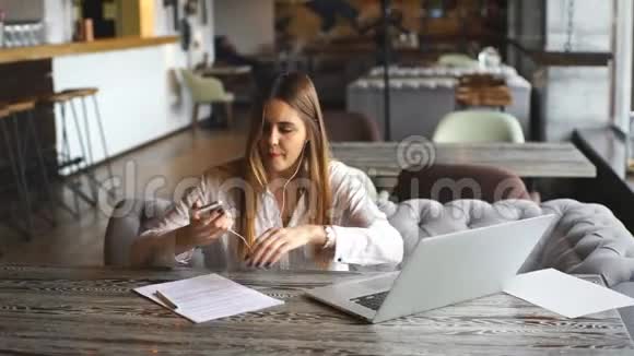 美丽的商务女性在文件上签名在耳机上听音乐视频的预览图