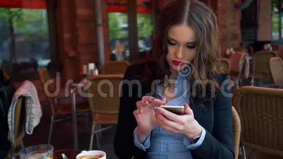 年轻貌美的女士在餐厅露台上吃早餐时会看到智能手机屏幕视频的预览图