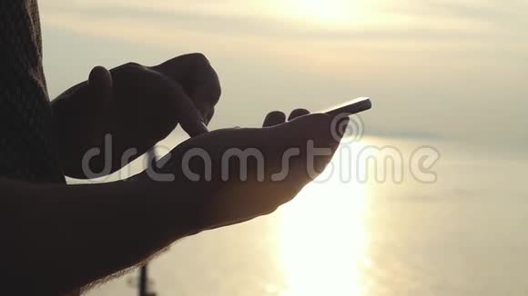 接近男性手使用触摸电话在金色日落海滩慢动作1920x1080视频的预览图