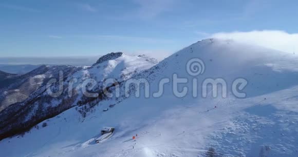 落后的空中冬季雪山山顶滑雪道度假村与滑雪者滑雪晴天雾蒙蒙的云福克视频的预览图