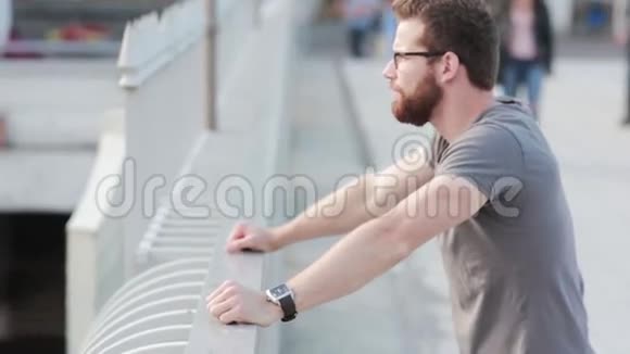 站在桥上的时髦男人带着胡子和眼镜的年轻商人在外面休息一下看着城市视频的预览图