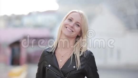 年轻微笑的女人看镜头的肖像快乐的金发女孩站在街上享受阳光明媚的一天视频的预览图
