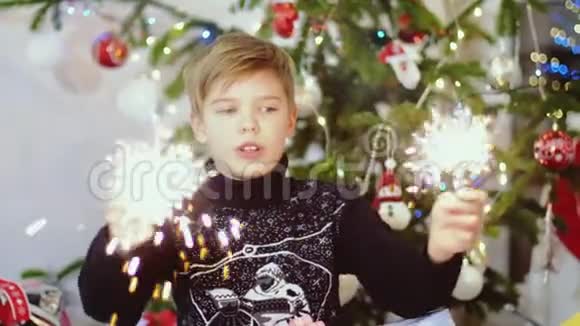 快乐的孩子在圣诞树上的bokeh灯和花环之间燃烧着火花慢动作3840x21604k视频的预览图