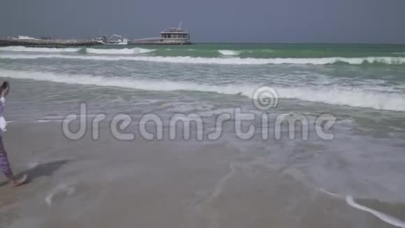 年轻女孩在迪拜海滩上的智能手机上拍摄波斯湾海浪的照片视频的预览图