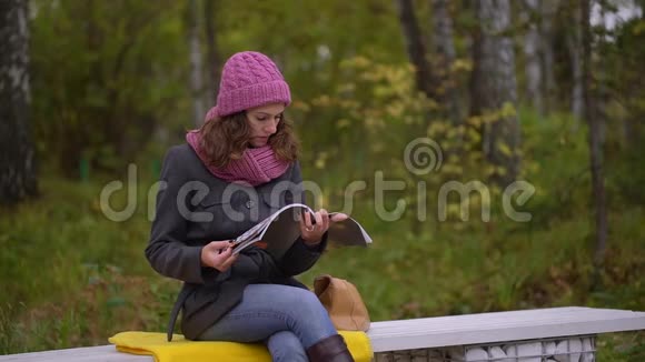 秋天一位年轻漂亮的女人在公园里读日记在秋天公园里放松阅读日志视频的预览图