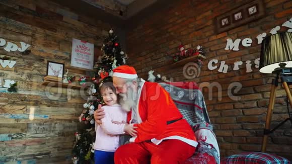在圣诞装饰的房间里快乐的女孩和圣诞老人紧紧拥抱在一起视频的预览图