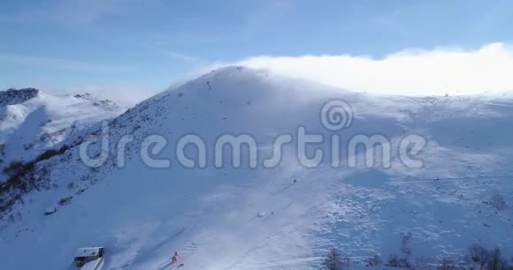 轨道航空飞越冬季雪山山顶滑雪道度假村与滑雪者滑雪晴天雾蒙蒙的云雾升起了视频的预览图