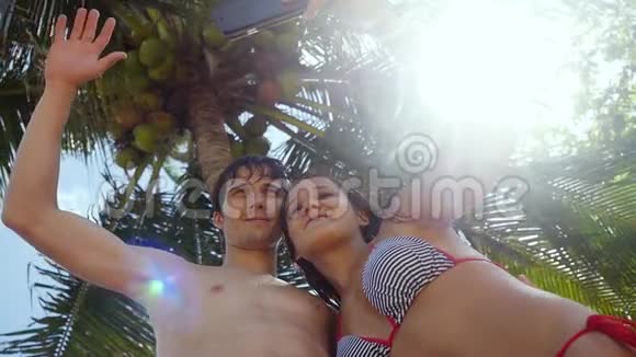 浪漫的幸福夫妻在阳光下在户外的棕榈树和阳光下在手机上自拍视频的预览图
