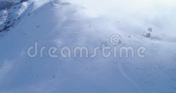 侧面空中飞越冬季雪山山顶滑雪道度假村与滑雪者滑雪晴天雾蒙蒙的云雾升起了视频的预览图