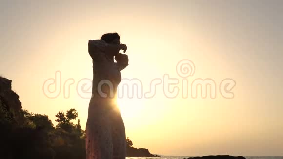 可爱的白种人布鲁内特女孩穿着轻装在日出时在海上悬崖跳舞视频的预览图