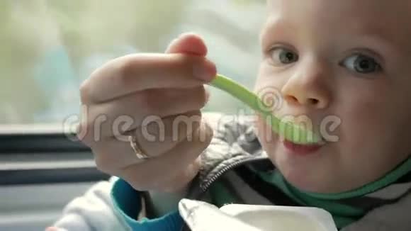 妈妈在靠近窗户的移动火车上喂婴儿妈妈用塑料勺子把粥递儿子的嘴里视频的预览图