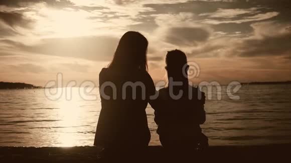 日落时分母亲和女儿坐在海滩上友好家庭观念生活方式视频的预览图