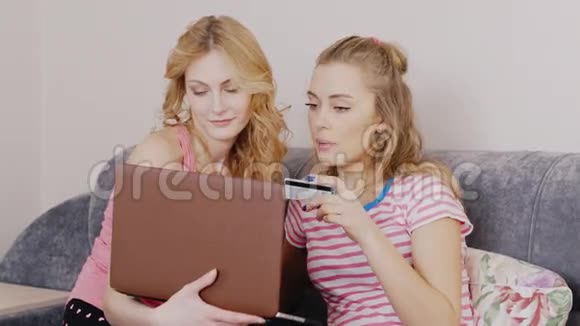 两个朋友在网上购物年轻女子坐在沙发上手里拿着一张信用卡视频的预览图