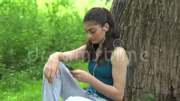 美丽的体育女孩带着电话在公园视频的预览图