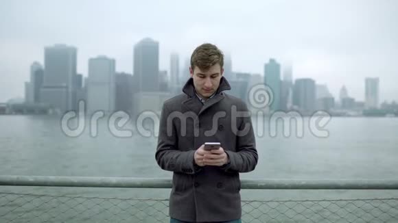 年轻人在哈德逊河附近发短信远处可以看到曼哈顿岛视频的预览图