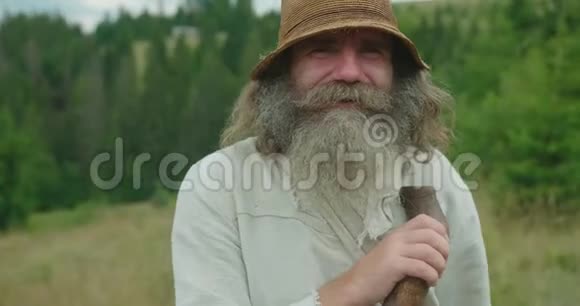 这位微笑的老人的特写肖像他的长发和胡须靠在拐杖上山的位置视频的预览图
