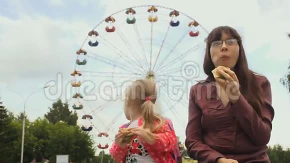 在夏天妈妈和女儿在摩天轮旁边吃汉堡视频的预览图