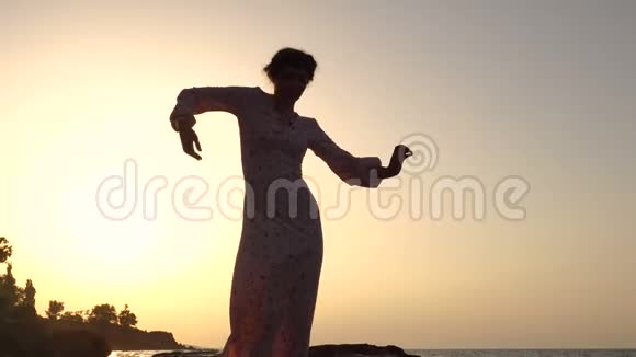 可爱的白种人布鲁内特女孩穿着轻装在日出时在海上悬崖跳舞视频的预览图