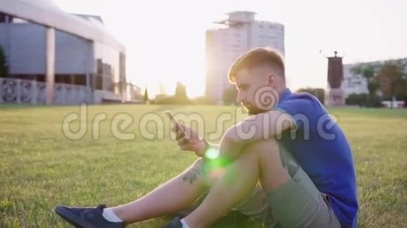 一个人坐在草地上翻着智能手机视频的预览图