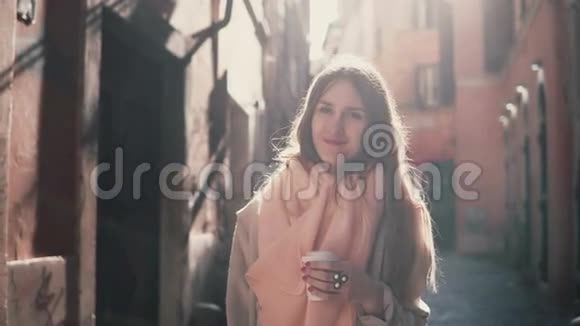 年轻微笑的女人看镜头的肖像快乐的黑发女孩站在早晨的街道上喝咖啡视频的预览图