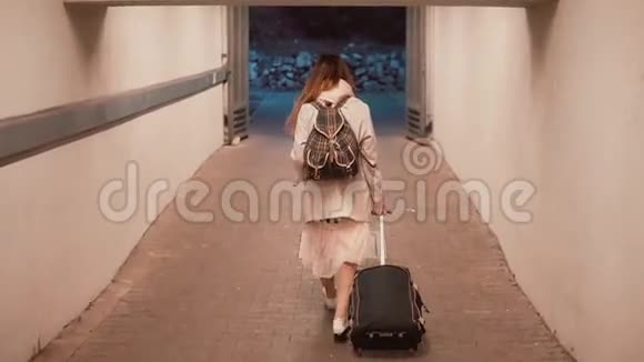 年轻女子提着手提箱穿过隧道带背包的女孩走在城市里旅行慢动作视频的预览图