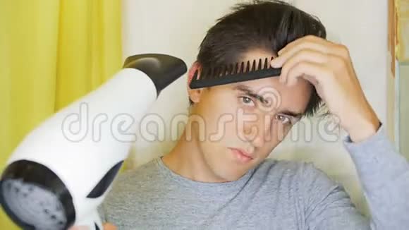 一个年轻人正在用吹风机烘干他的头发视频的预览图