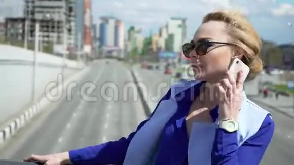 美丽的金发商务女性穿着蓝色西装走在一个明亮温暖的城市摆姿势在车桥上视频的预览图
