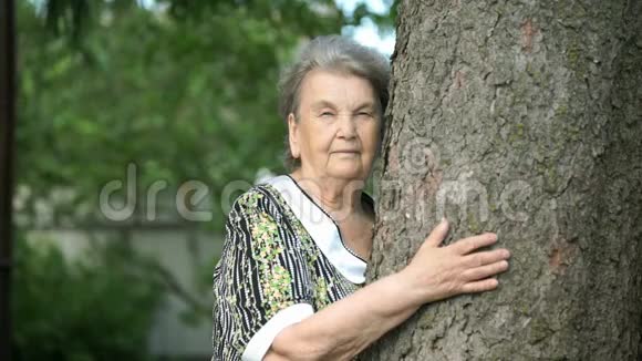 一位抱着树微笑的老妇人在镜头前视频的预览图