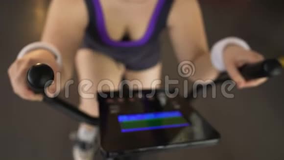 肥胖妇女骑着固定自行车看电子面板运动视频的预览图