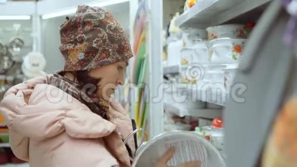 美丽的女人穿着头饰和羽绒服在商店里选择一个平底锅选择和购买视频的预览图