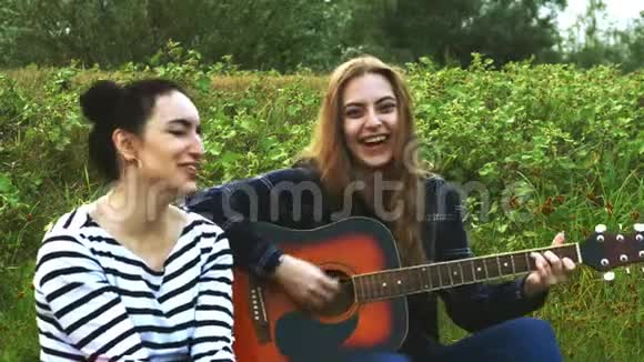 两个美丽的年轻时髦女孩高兴地唱吉他歌曲4K视频的预览图