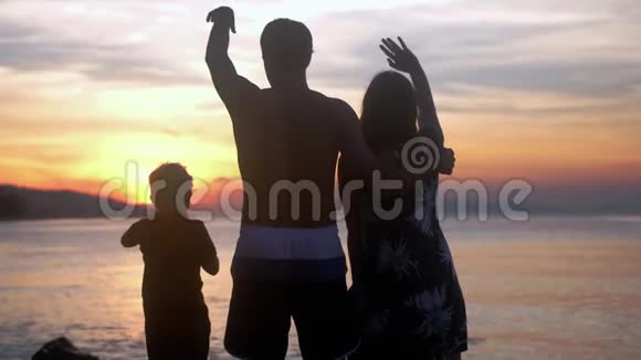 年轻快乐的一家人在暑假拥抱在热带海滩美丽的日落时挥手慢动作视频的预览图