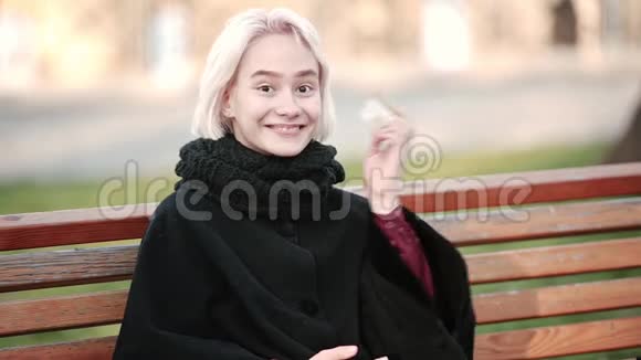 一个女人拿着智能手机和一张黄金信用卡坐在长凳上向人们展示了一张支付卡的快乐视频的预览图