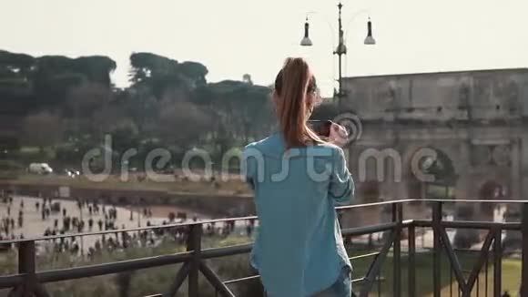 游客深色头发的女人在意大利罗马用智能手机拍摄君士坦丁拱门和竞技场的照片慢动作视频的预览图