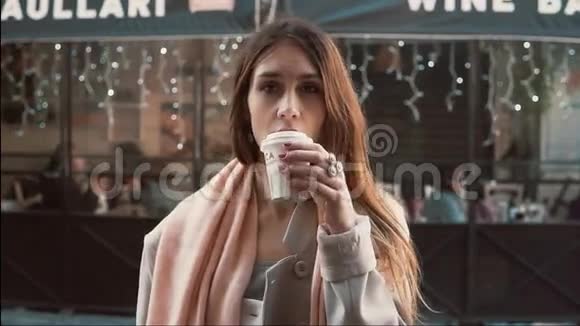 年轻的黑发女人端着一杯咖啡站在橱窗前女孩梦想着买衣服慢动作视频的预览图