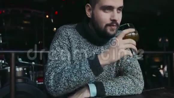 年轻迷人的蓝眼大胡子男人穿着一件温暖的毛衣喝着啤酒对味道感到惊讶目光正朝着视频的预览图