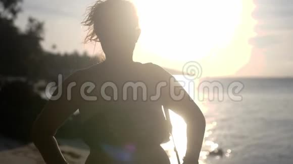 穿着比基尼和太阳镜的美丽年轻女子站在热带海滩上阳光照射着视频的预览图