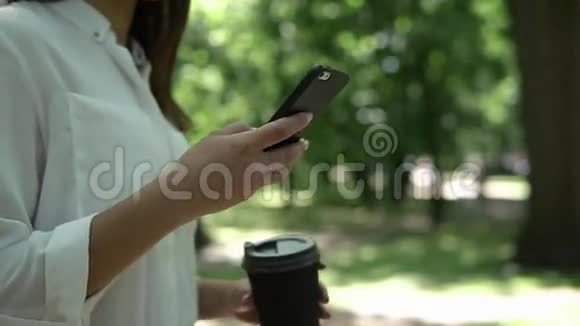 女人在公园里用咖啡检查她的手机视频的预览图