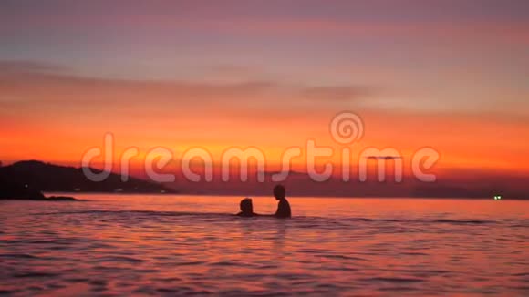 在美丽的夕阳下父亲和小儿子在海里洗澡用手缓慢地挥动着视频的预览图