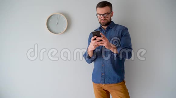 一个长胡子的人用智能手机对着灰色的墙挂着一只钟视频的预览图