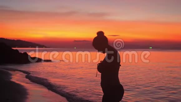 穿比基尼的年轻女人的剪影喜欢在可爱的日落海滩上散步慢动作3840x2160视频的预览图