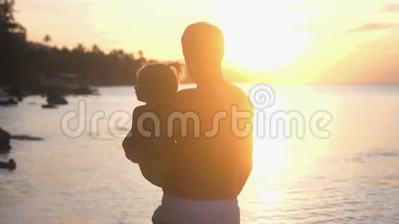 父亲抱着他的小女孩散步在美丽的日落时在海滩上聊天慢动作的镜头闪光效果视频的预览图