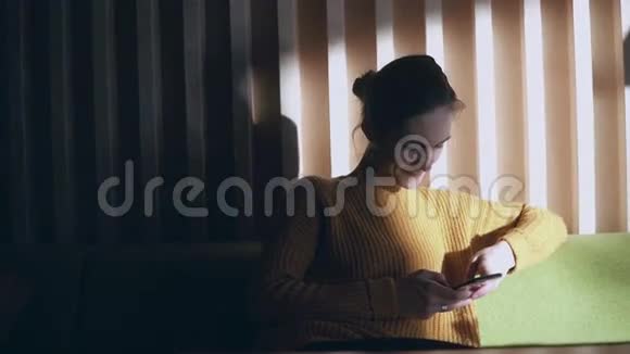 年轻微笑的女人坐在沙发上用智能手机的肖像女孩早上上网视频的预览图