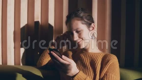 年轻迷人的女人坐在沙发上用智能手机美丽的女孩早上上网视频的预览图
