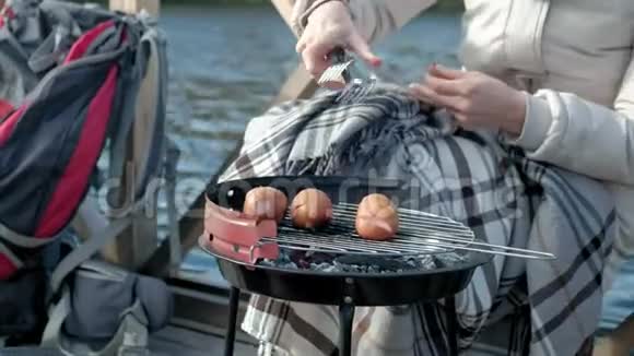 女游客穿着温暖的衣服在河岸边的桥上背着背包准备烤架上的香肠野餐视频的预览图