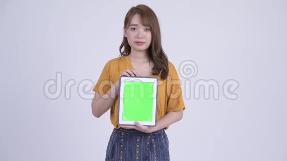 快乐年轻美丽的亚洲女人一边思考一边展示数码平板电脑视频的预览图