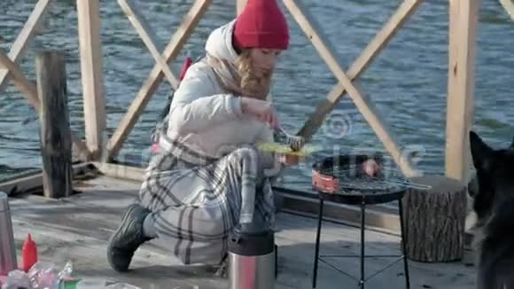 女游客穿着温暖的衣服在河岸边的桥上背着背包准备烤架上的香肠野餐视频的预览图