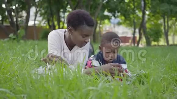 肖像可爱可爱的非裔美国人漂亮的年轻女人躺在毯子上和她的小儿子玩玩具视频的预览图